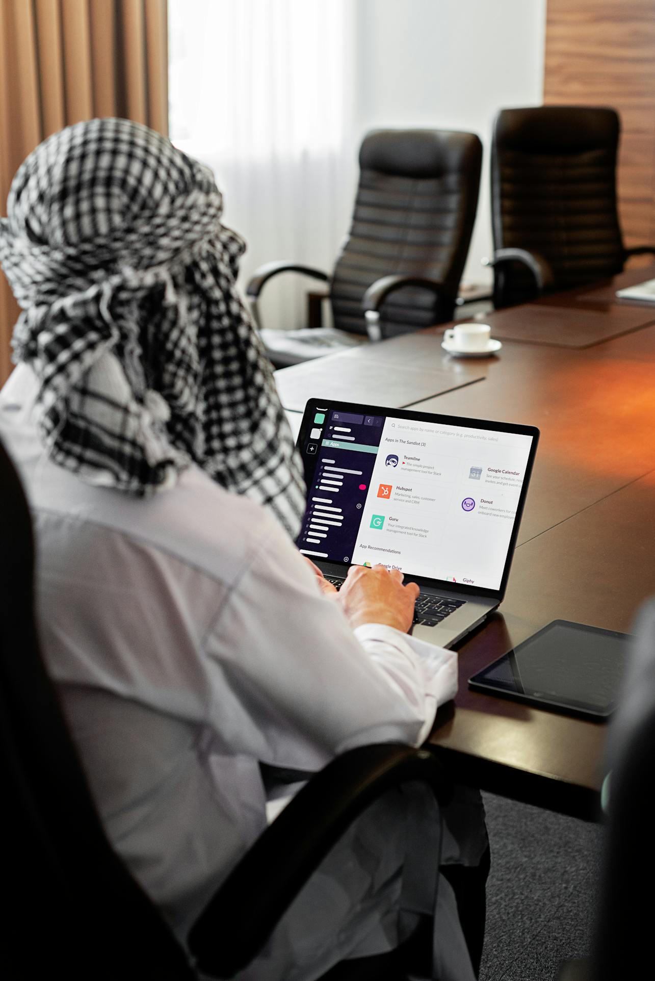 Middle Eastern man using a laptop with Slack in a modern office meeting room.